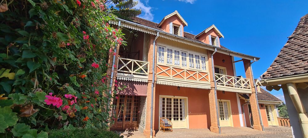 Façade à véranda de Tsara Guest House, briques apparentes, toit de tuiles et balustrades de bois.